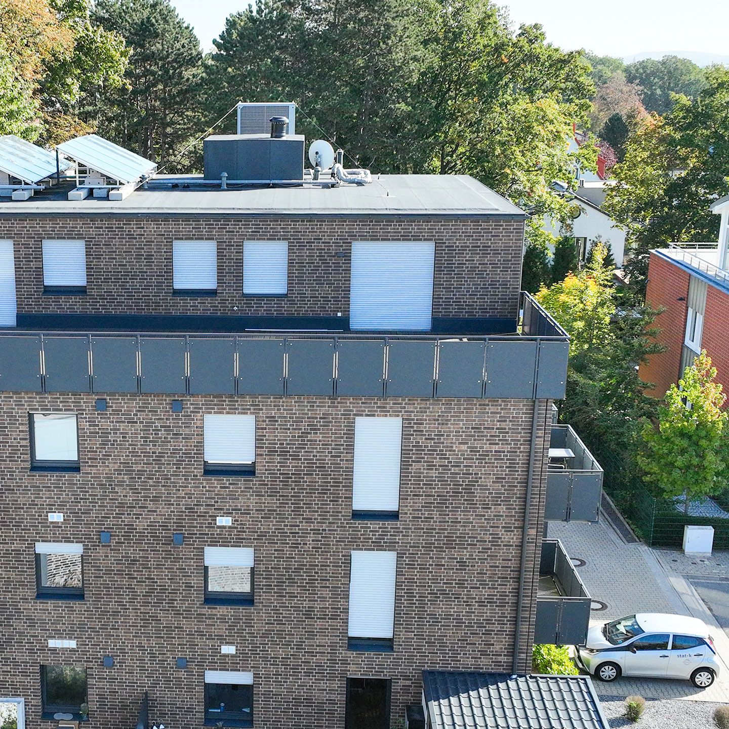 Modernes mehrstöckiges Wohngebäude mit Solarpaneelen auf dem Dach, umgeben von grüner Umgebung.