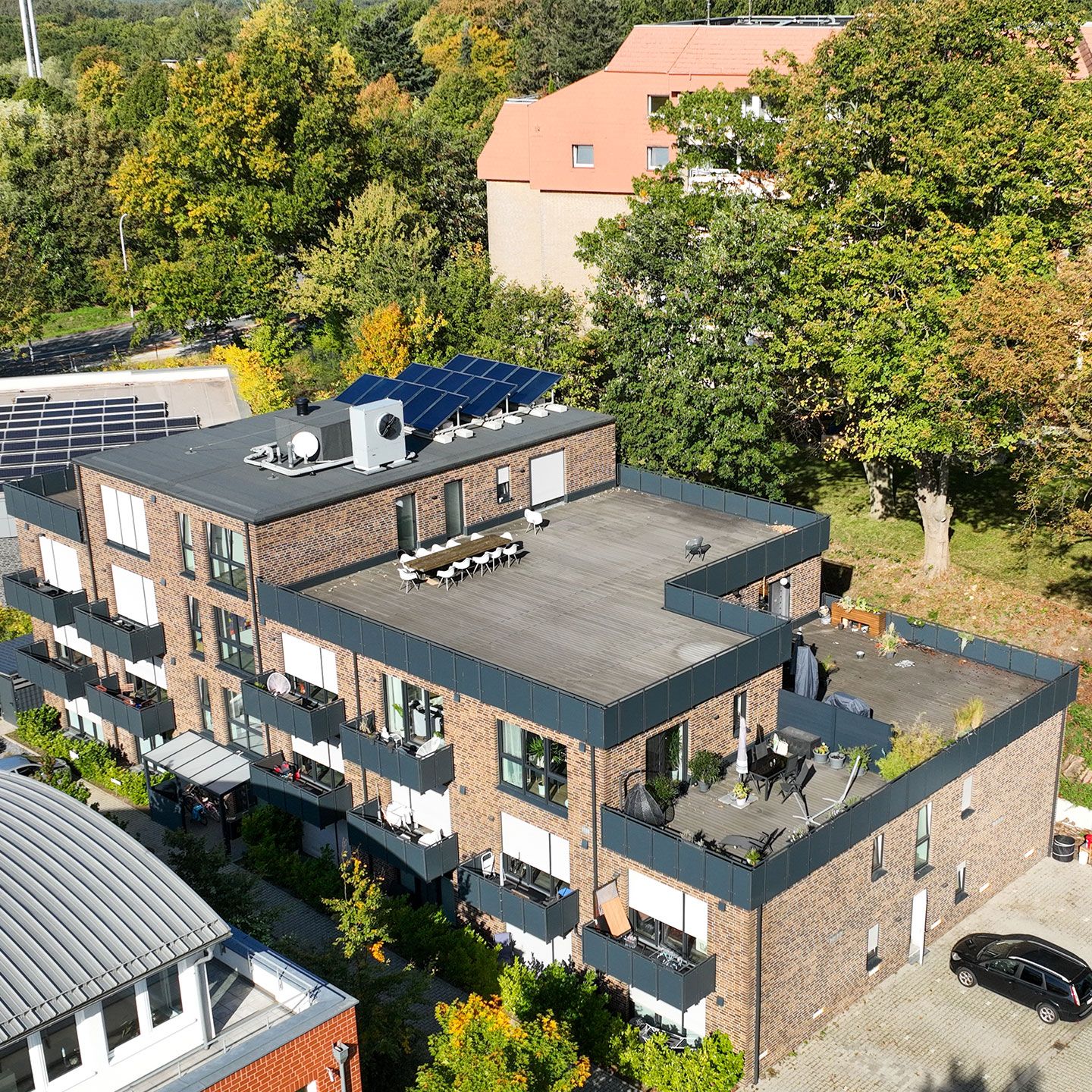 Modernes Wohngebäude mit Solarpaneelen auf dem Dach, umgeben von grüner Vegetation und einem Auto.