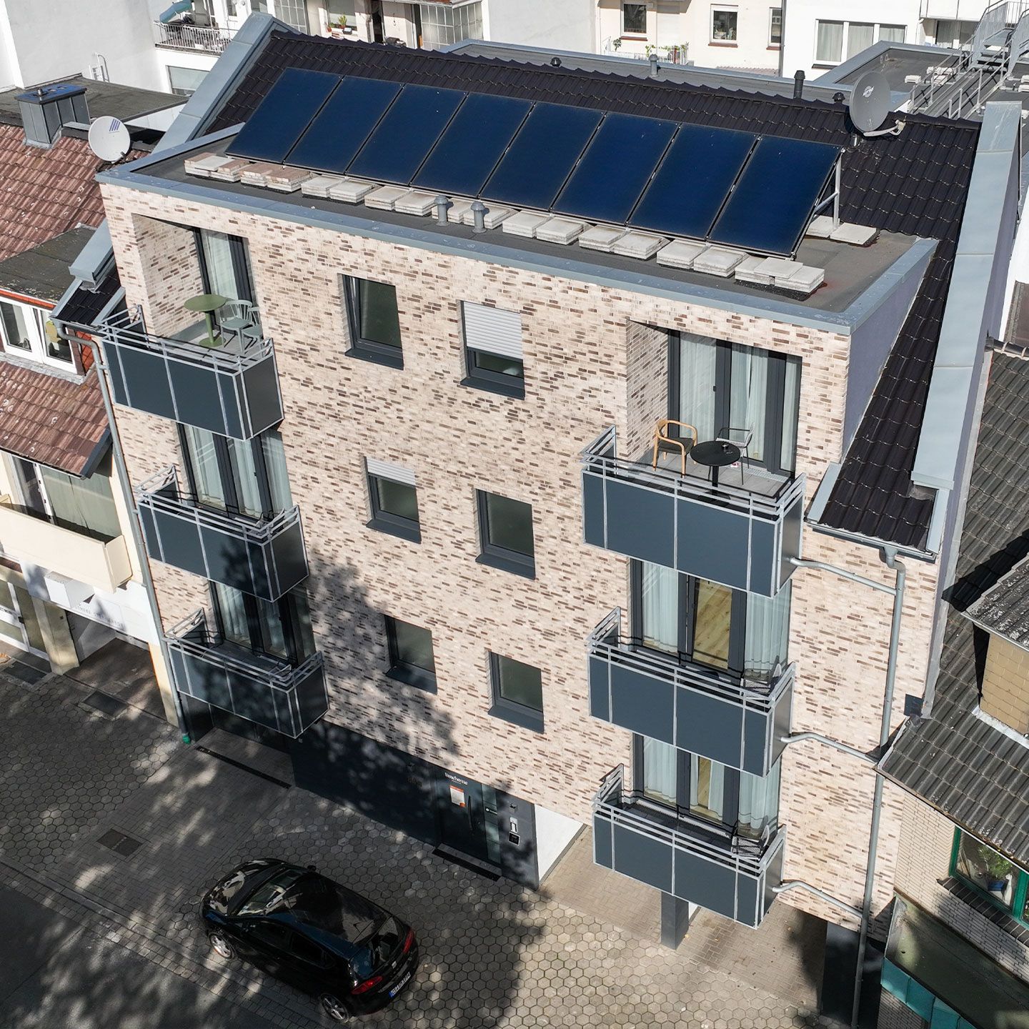 Modernes Wohngebäude mit heller Ziegelfassade, Balkonen und Solarpaneelen auf dem Dach.