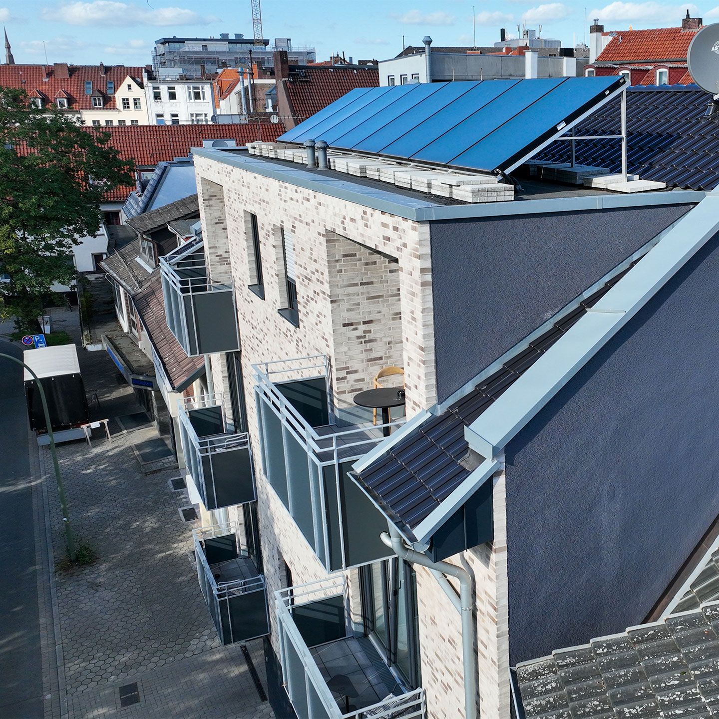 Moderne Wohngebäude mit Solarpaneelen auf dem Dach, umgeben von weiteren Gebäuden und einer Straße.