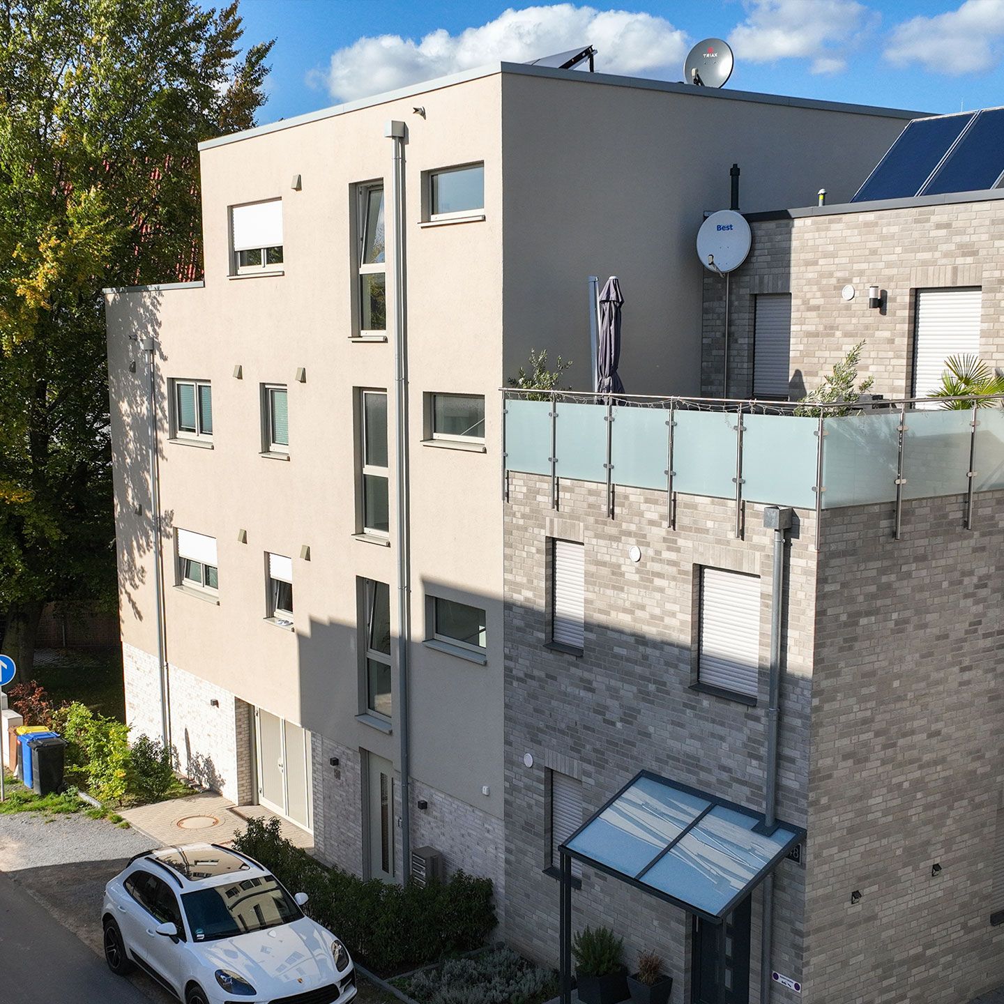 Modernes Wohngebäude mit glatter Fassade, Ziegelwänden, Balkon, weißem Auto und Satellitenschüsseln.