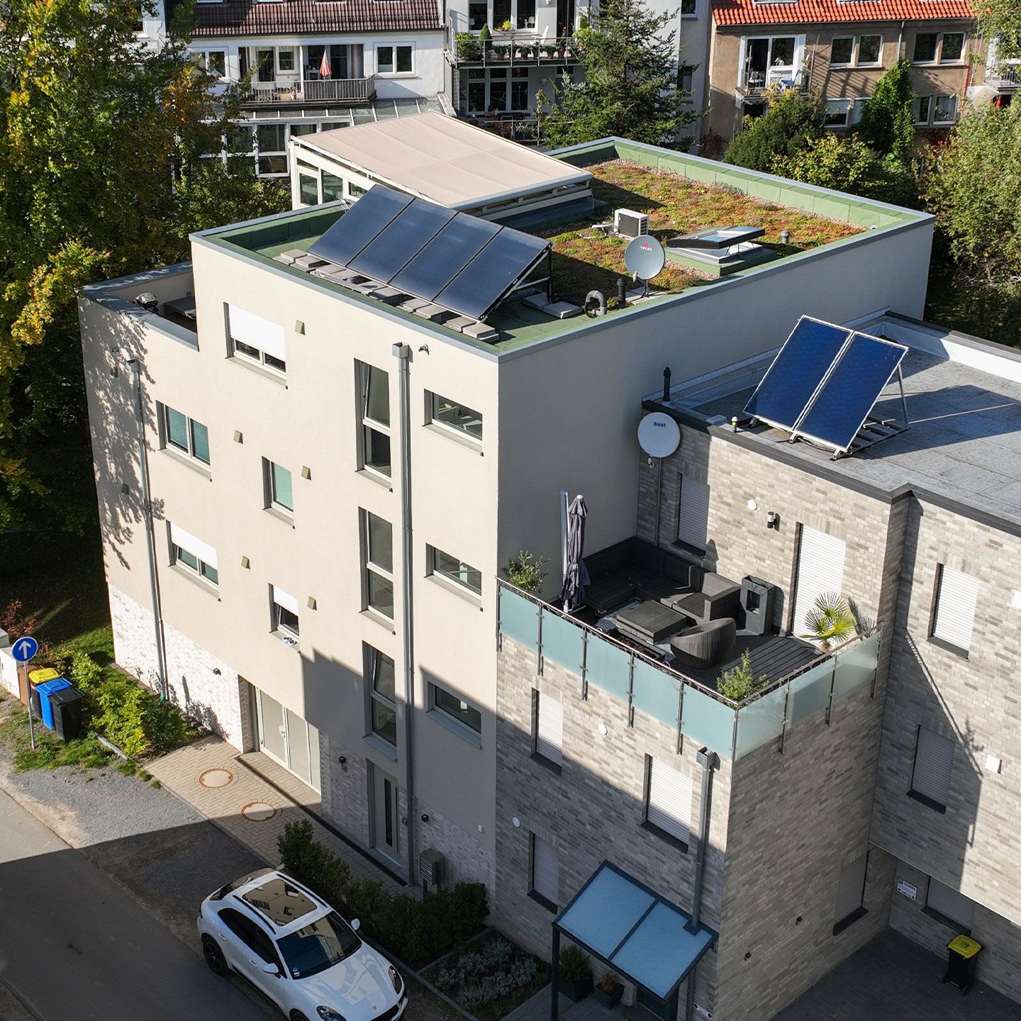 Modernes Wohngebäude mit Solarpaneelen, Dachbegrünung und Balkon; herbstliche Umgebung.