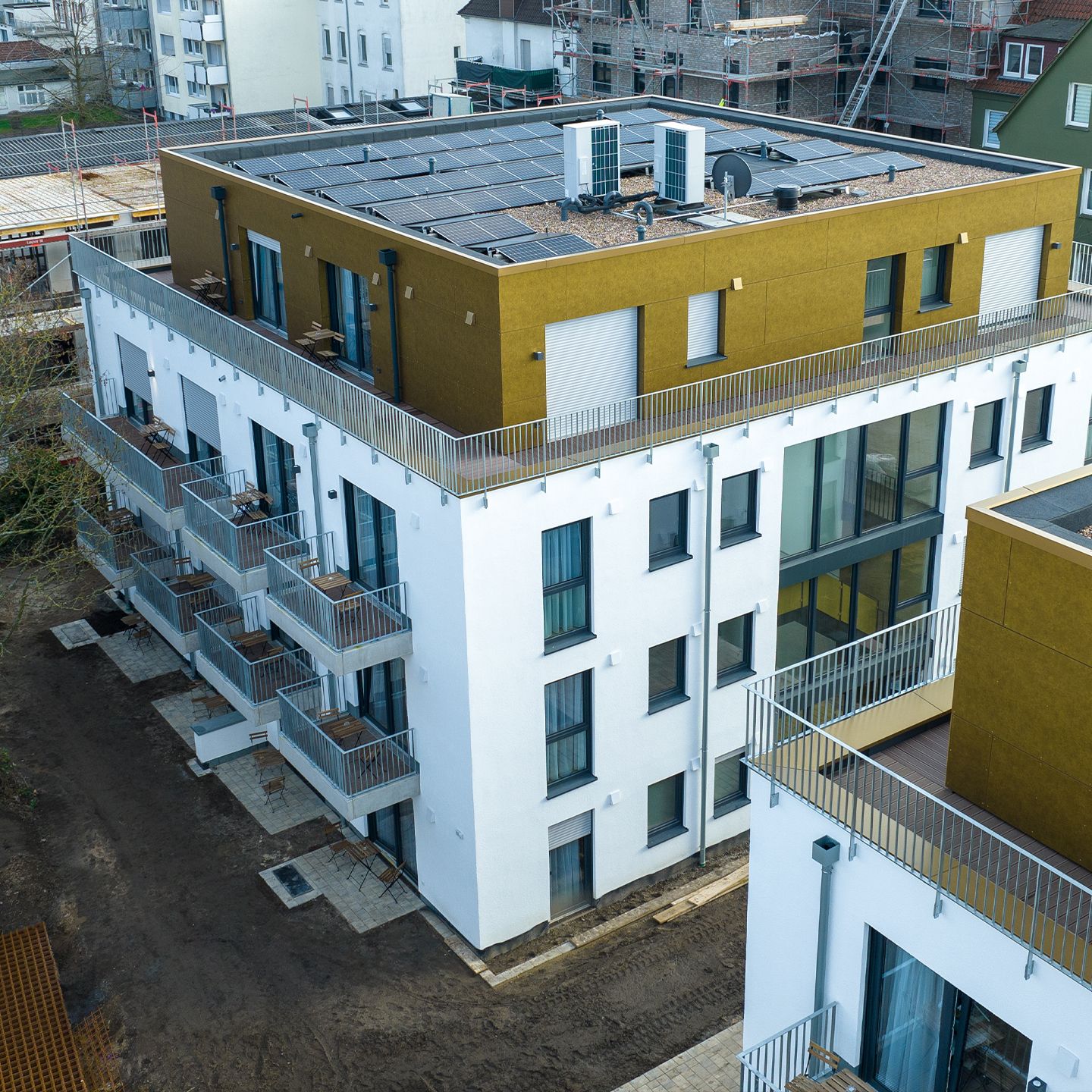 Modernes Wohngebäude mit weißer Fassade, Solarpaneelen auf dem Dach und Balkonen in urbaner Umgebung.