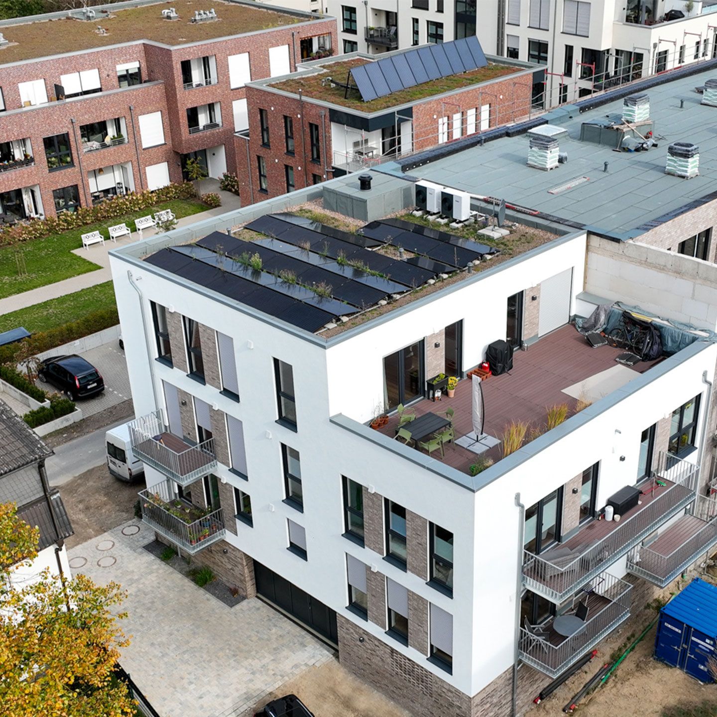 Modernes Wohngebäude mit Solarpanels und begrünten Dächern, Balkonen und Dachterrasse in urbaner Umgebung.