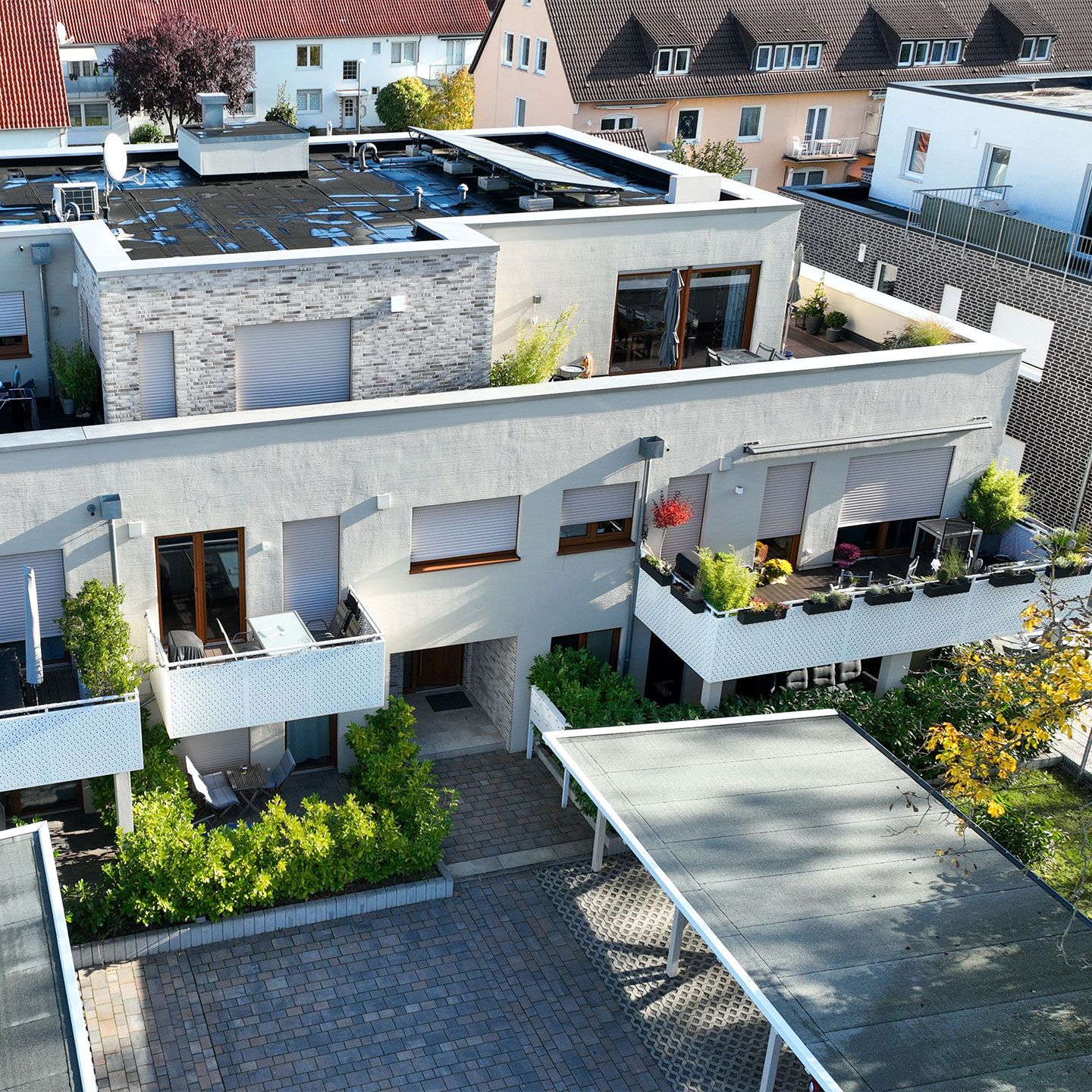 Modernes Wohngebäude mit neutraler Fassade, Balkonen mit Pflanzen und einem gepflasterten Hof.