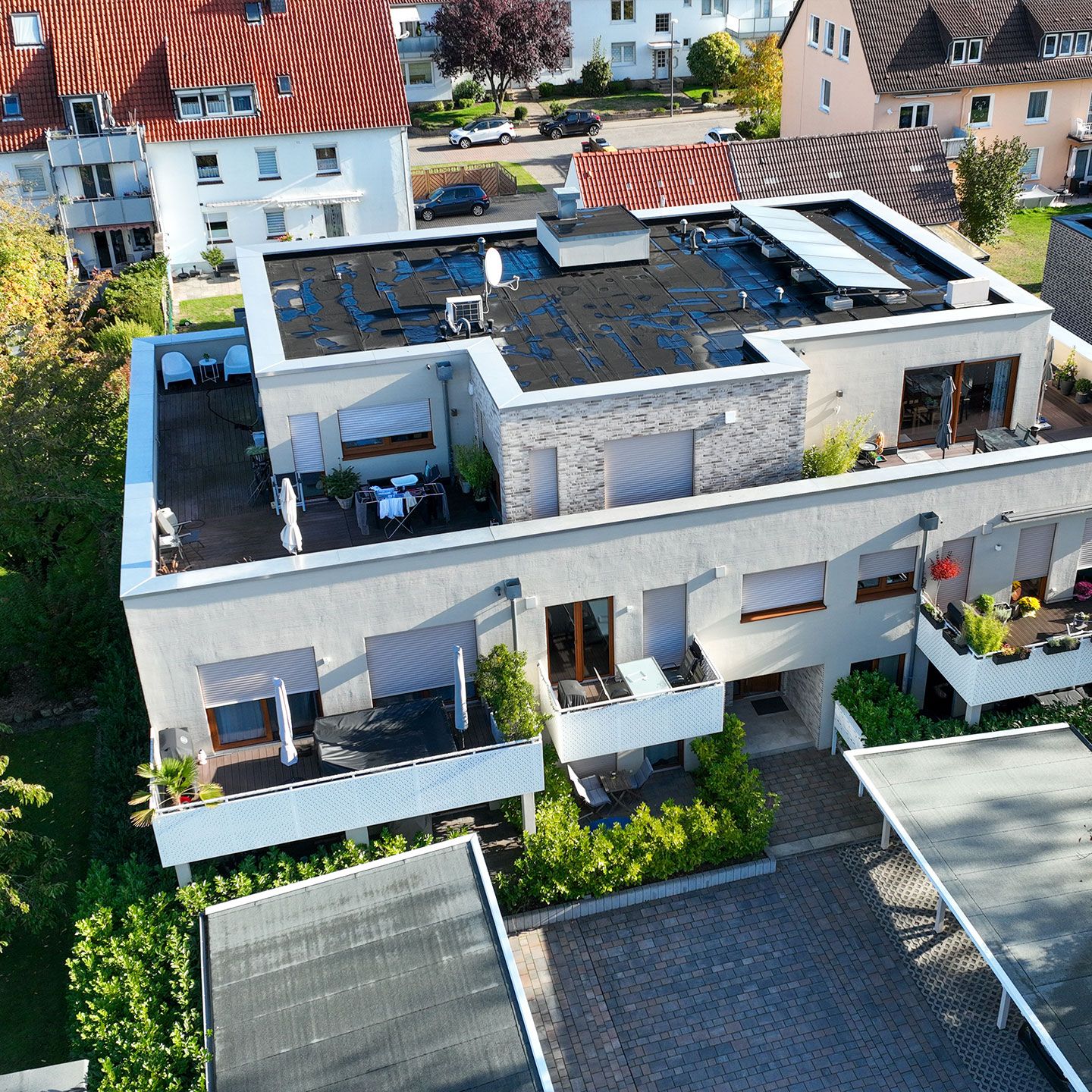 Moderne Wohnanlage mit Flachdach, Balkonen, Dachterrasse und grüner Umgebung bei sonnigem Wetter.