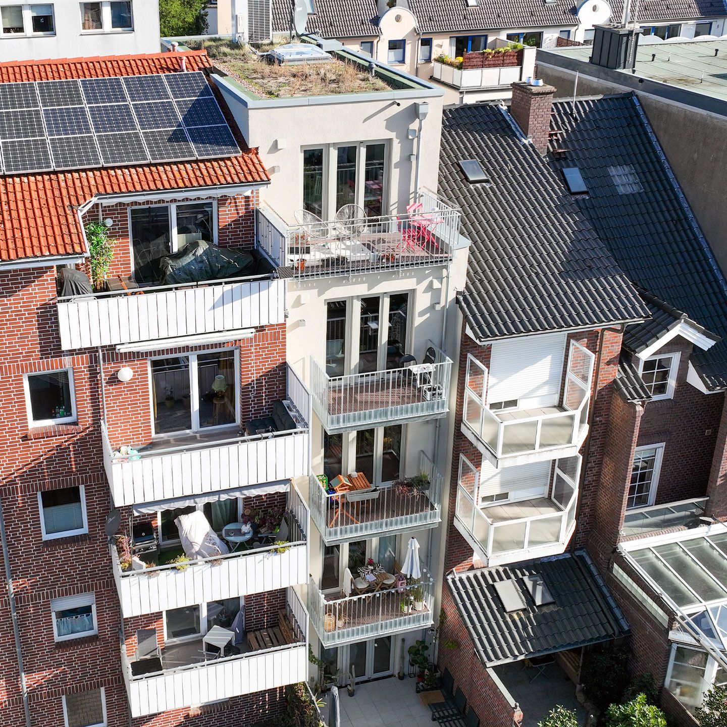 Mehrstöckiges Wohngebäude mit roten Ziegelwänden, Balkonen mit Pflanzen und Solarpanels auf dem Dach.