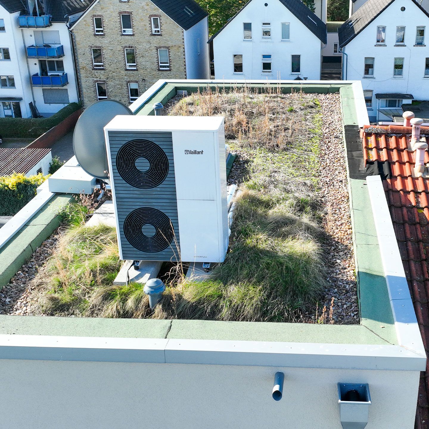 Ein begrüntes Flachdach mit Klimagerät und Satellitenschüssel in städtischer Umgebung.