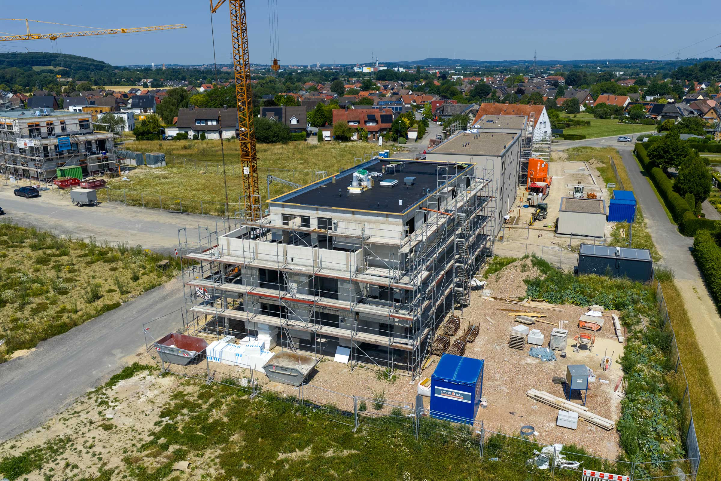 Städtische Baustelle mit Gebäude im Bau, umgeben von Gerüsten und einem großen Kran unter blauem Himmel.
