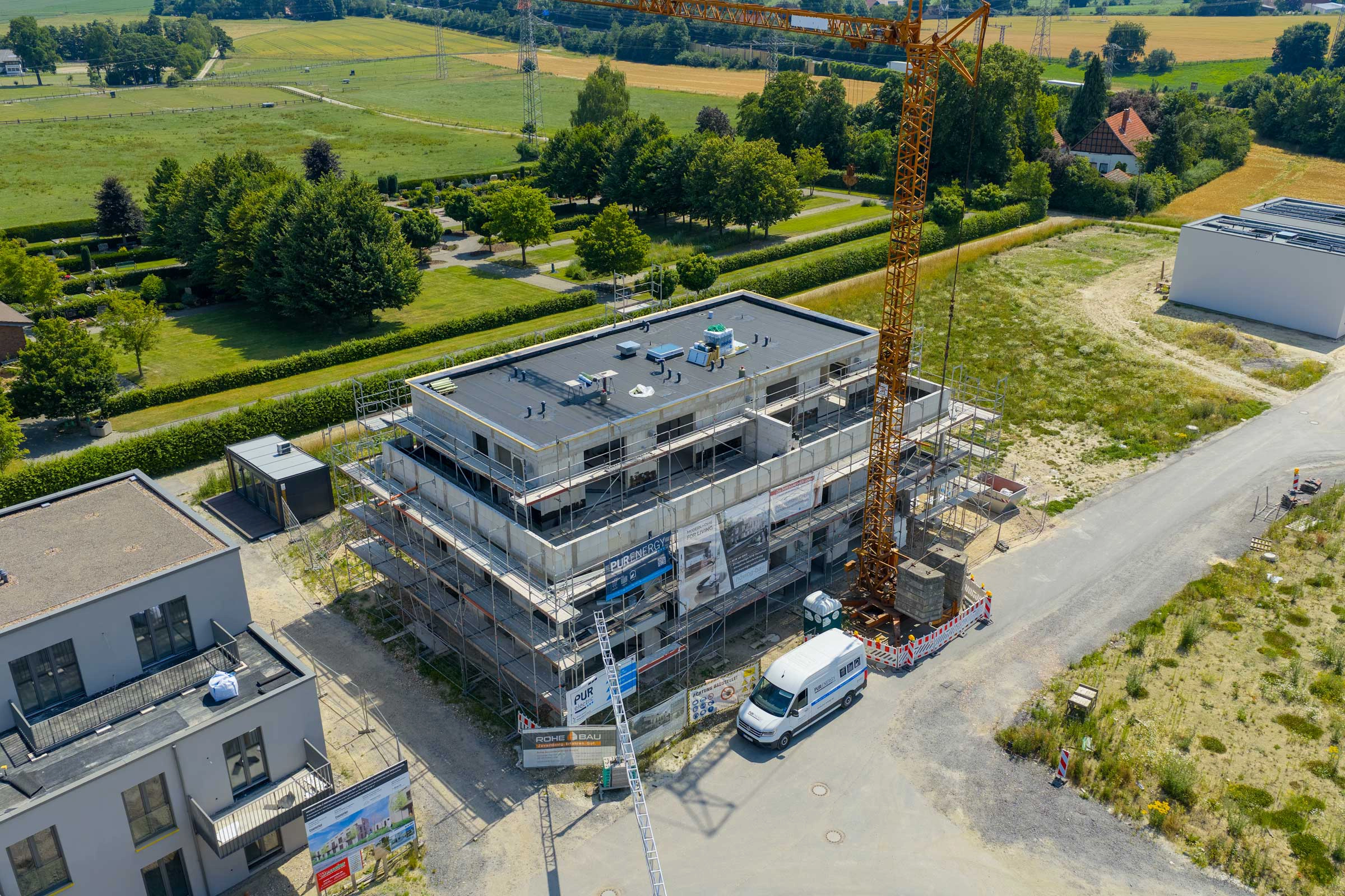 Baustelle in ländlicher Umgebung mit Gebäude im Bau, Baukran und geparktem Lieferwagen.
