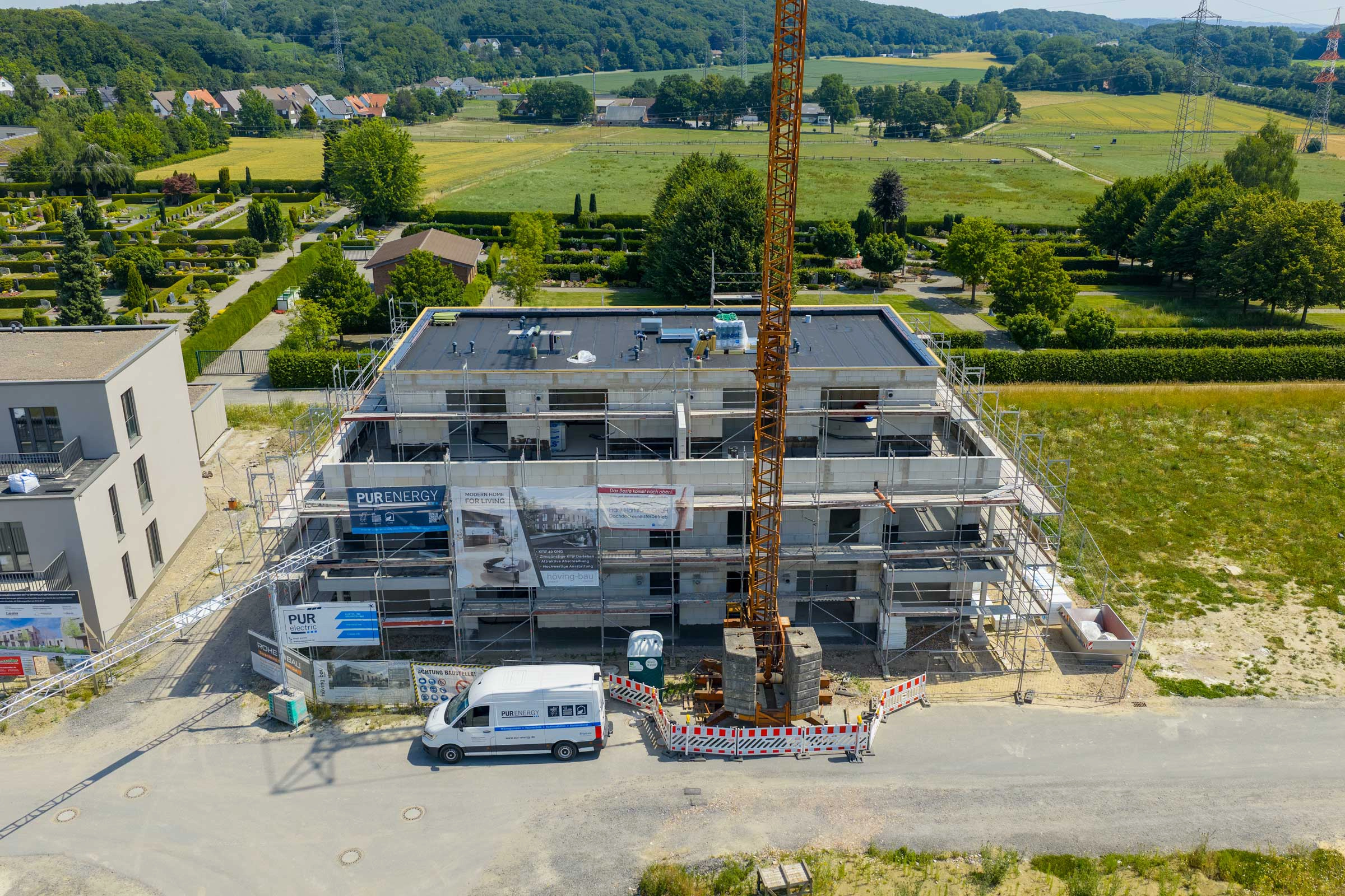 Eine ländliche Baustelle mit einem mehrstöckigen Gebäude, Baukran und einem weißen Lieferwagen.