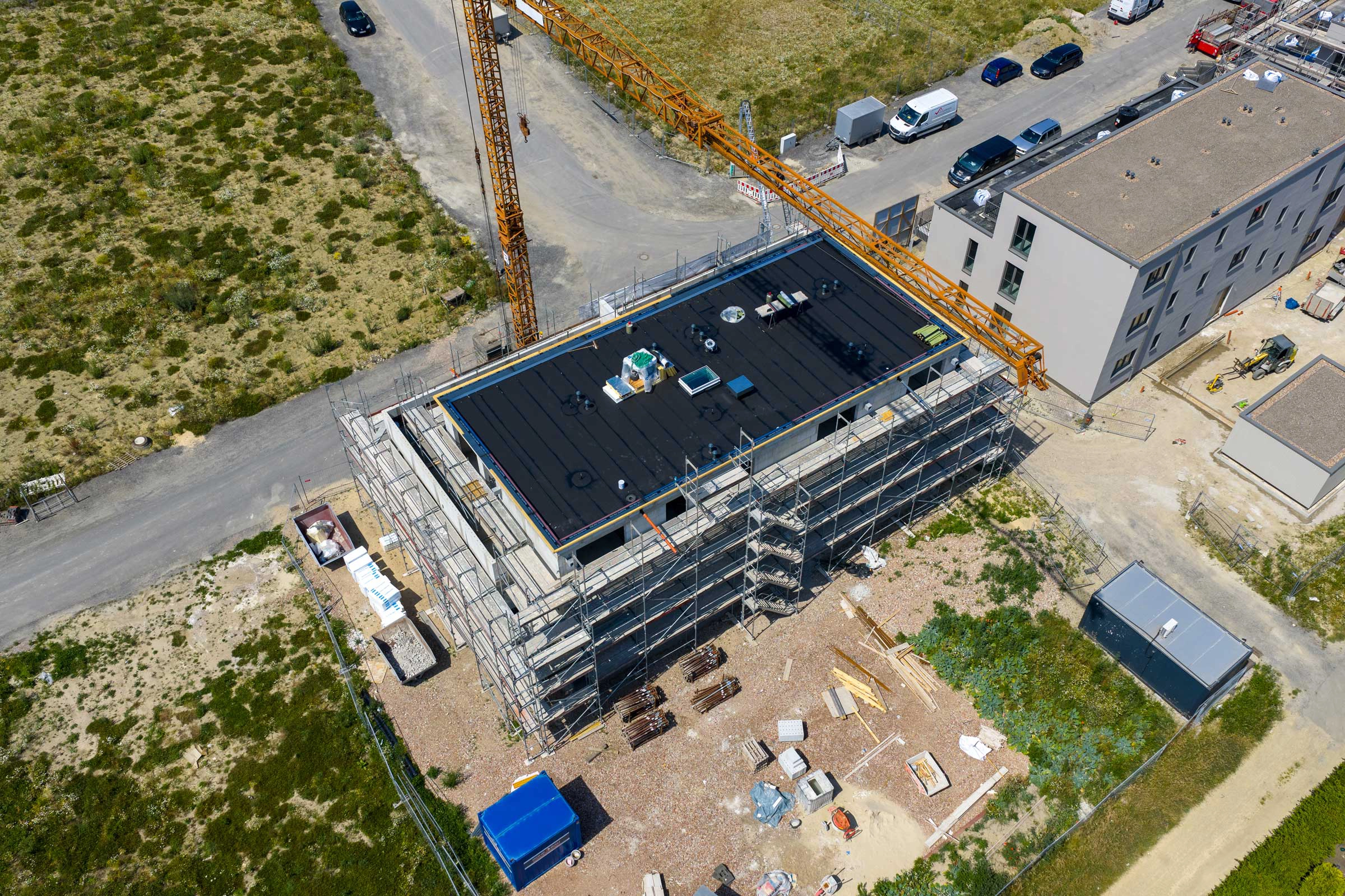 Vogelperspektive einer ruhigen Baustelle mit Baugerüst, Kran und verstreuten Materialien.