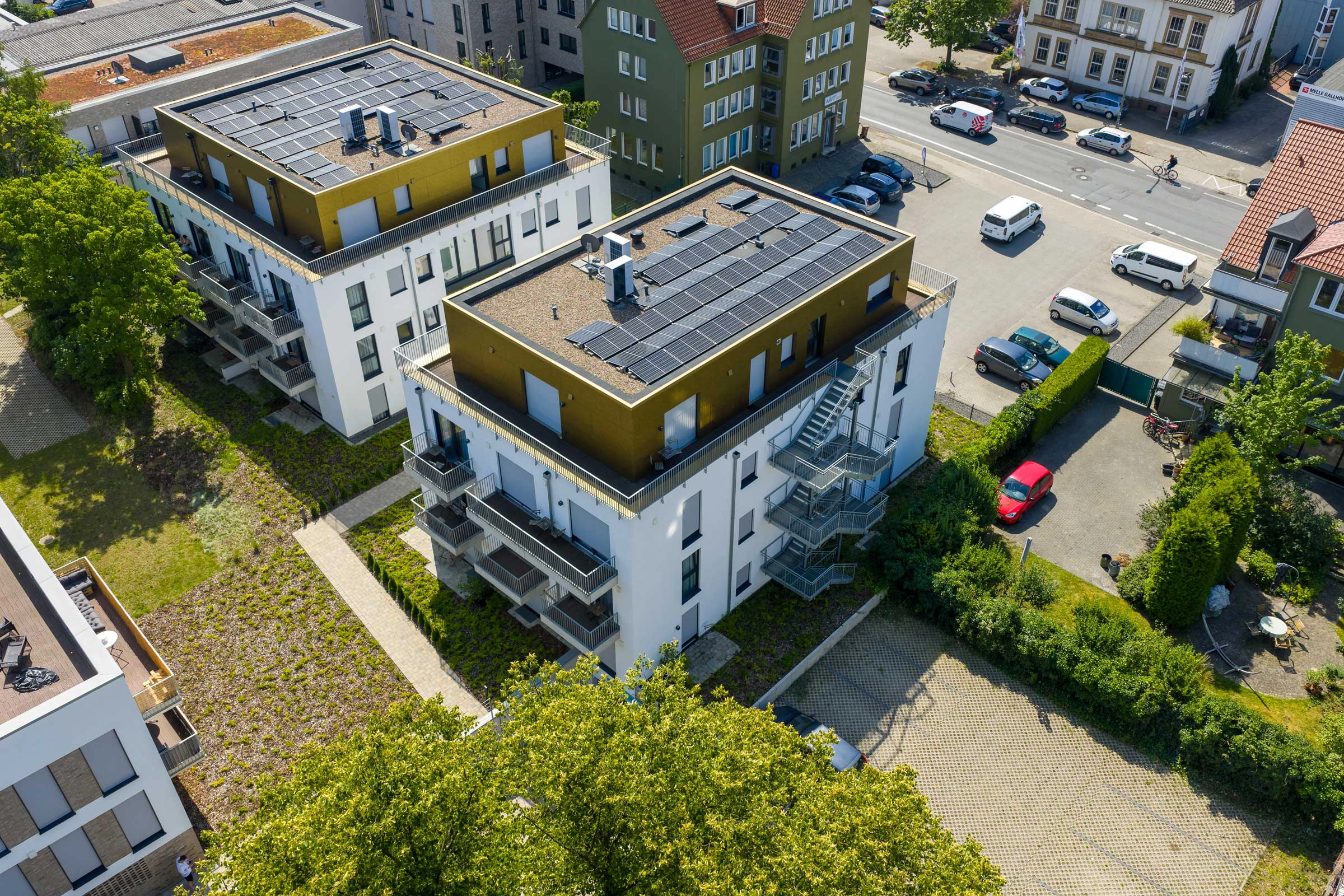 Moderne Wohngebäude mit Solarpaneelen, umgeben von Bäumen und geparkten Autos in einer ruhigen Straße.