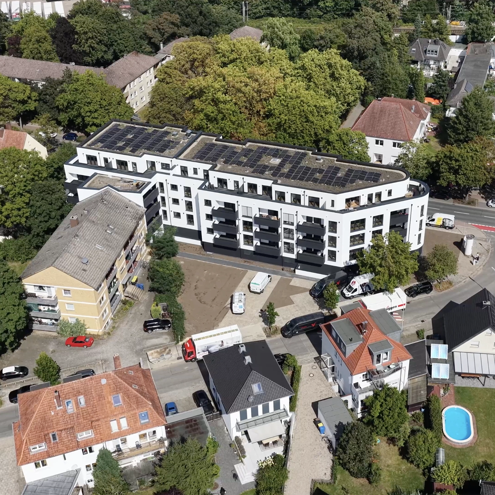 Luftaufnahme eines Wohngebiets mit modernen und älteren Häusern, Solarpanels und geparkten Fahrzeugen.