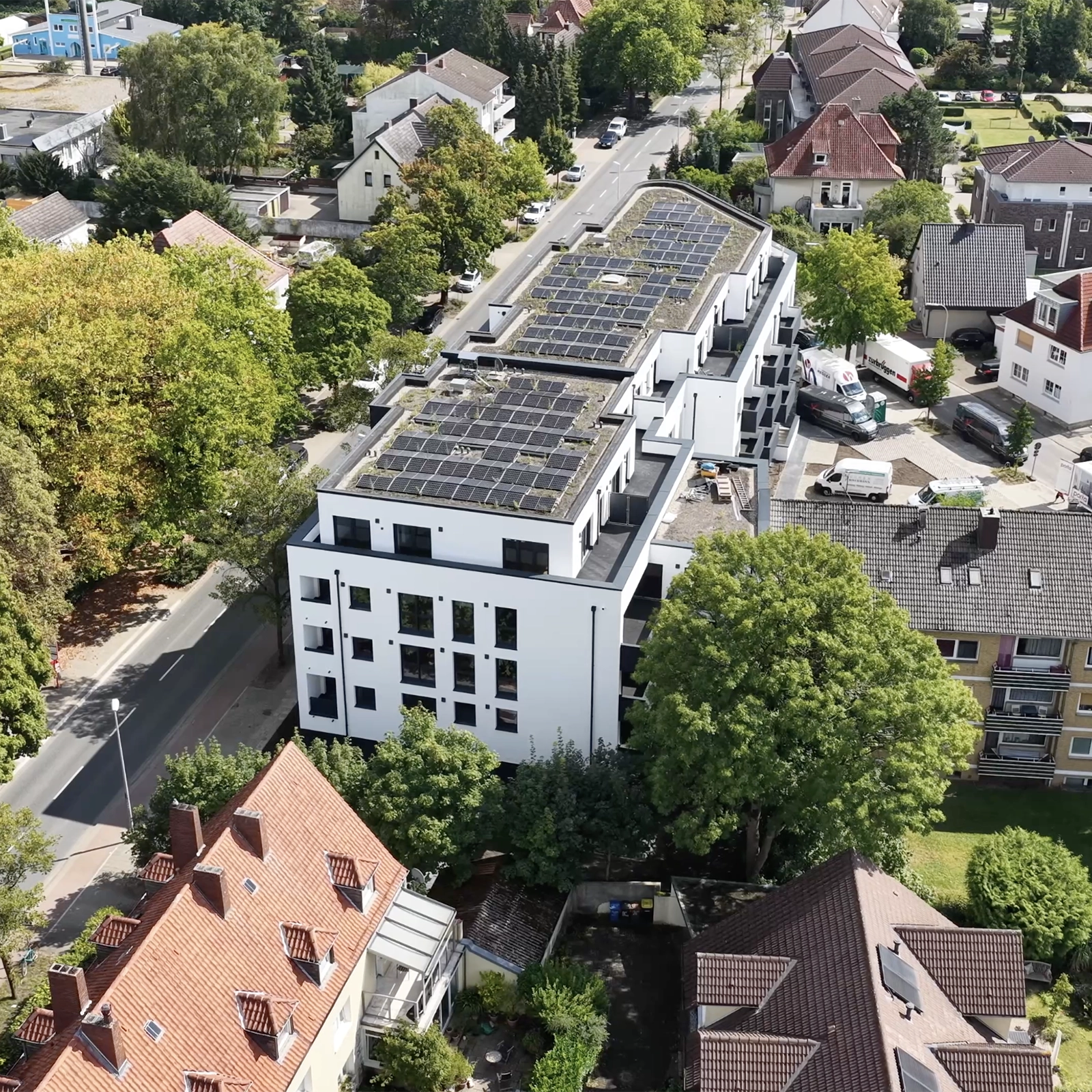 Vogelperspektive auf modernes Gebäude mit Solarpaneelen, umgeben von traditionellen Wohnhäusern.