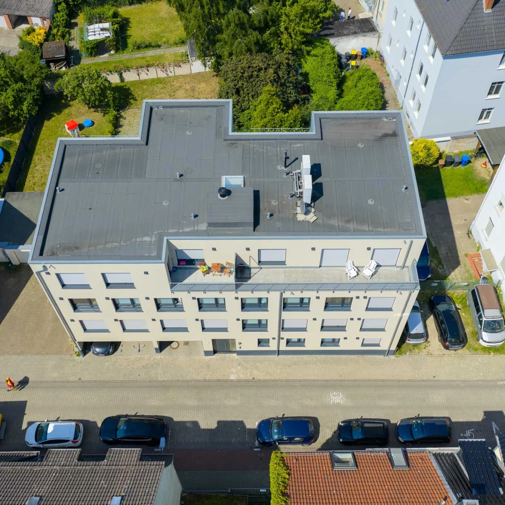 Vogelperspektive einer ruhigen Wohngegend mit modernem Gebäude, geparkten Autos und einem gelben Lieferwagen.