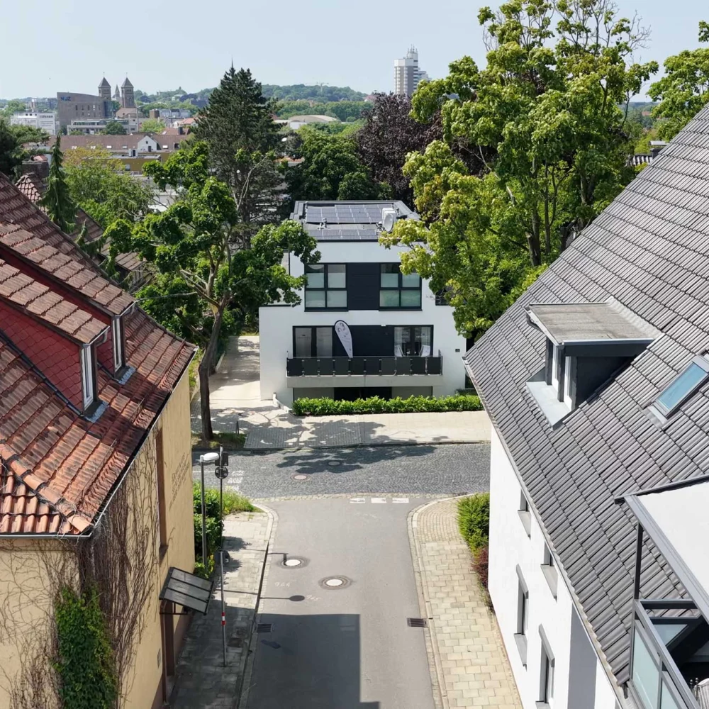 Städtische Szene mit traditionellen und modernen Häusern, Solarpanelen und grüner Vegetation an einem sonnigen Tag.