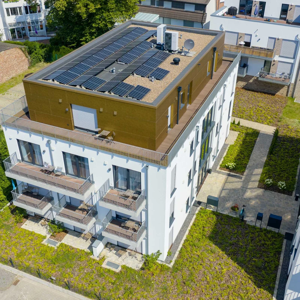 Moderne Wohnanlage mit Solarpaneelen, Balkonen und gepflegten Grünflächen, rotes Auto geparkt.