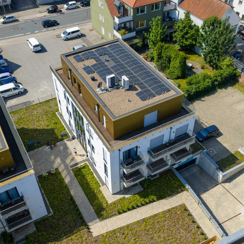 Vogelperspektive auf modernes Gebäude mit Solarpaneelen, geparkten Autos und Person auf dem Weg.