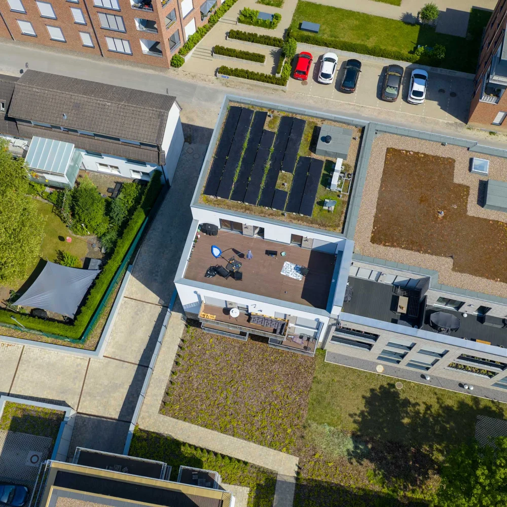 Luftaufnahme eines urbanen Wohngebiets mit Flachdachgebäuden, Solarpaneelen und einem kleinen Garten.