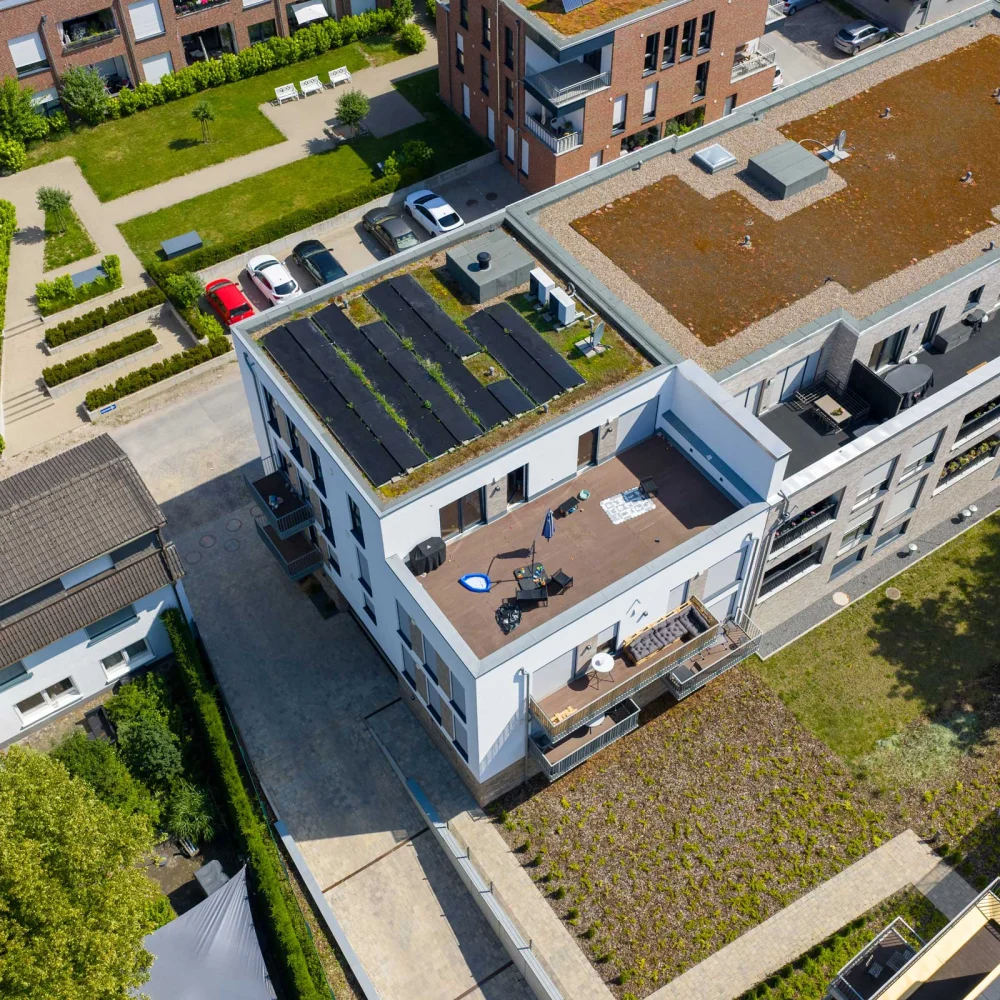Vogelperspektive auf modernes Wohngebiet mit begrünten Flachdächern und einer möblierten Dachterrasse.