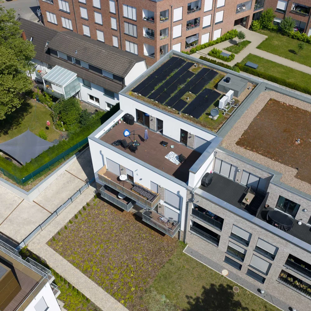 Moderne Wohngebäude mit begrünten Flachdächern, Solarpaneelen und Dachterrassen in urbaner Umgebung.