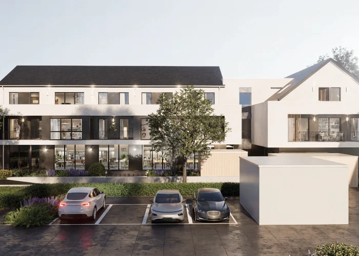 Modernes, dreistöckiges Gebäude mit geparkten Autos und einem großen Baum im Vordergrund. Eine Person steht auf einem Balkon.