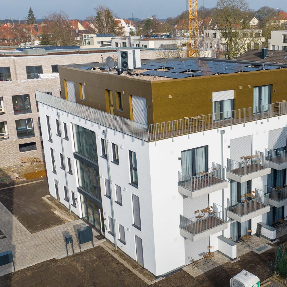 Modernes Wohngebäude mit weißen und braunen Fassaden, Balkonen und Solarpaneelen unter blauem Himmel.