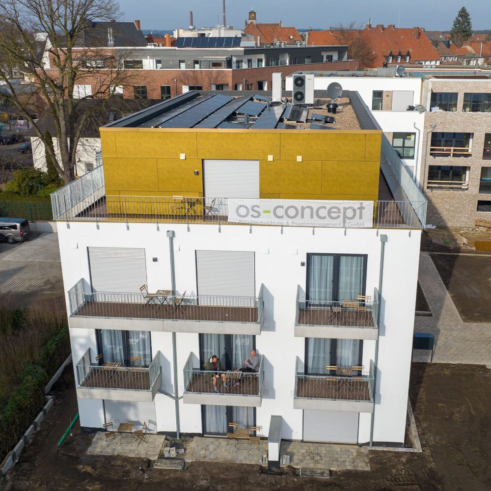 Modernes Gebäude mit weißer Fassade, gelbem Dachgeschoss, Solarpaneelen und Personen auf einem Balkon.