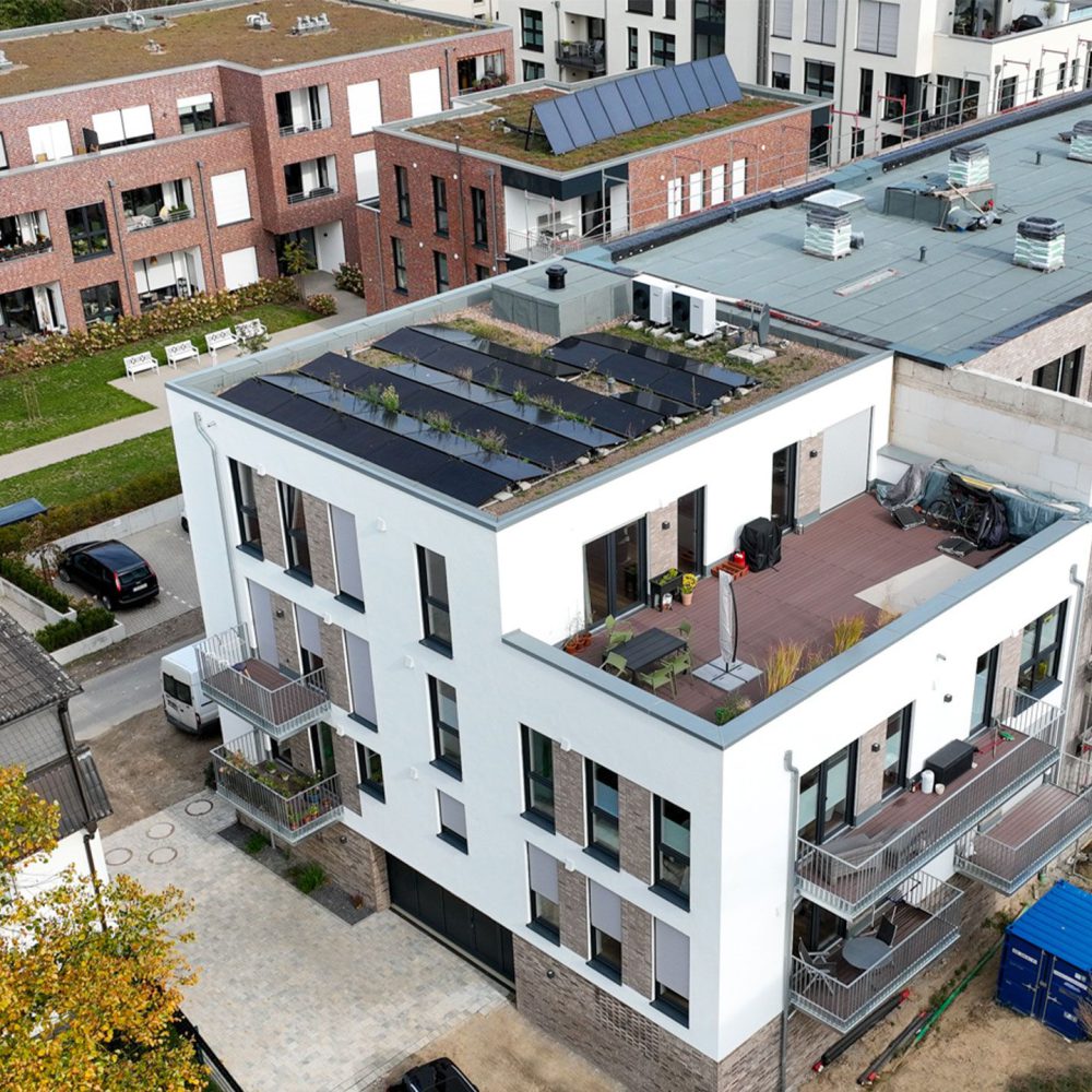 Modernes Wohngebäude mit Solarpanels und begrünten Dächern, Balkonen und Dachterrasse in urbaner Umgebung.
