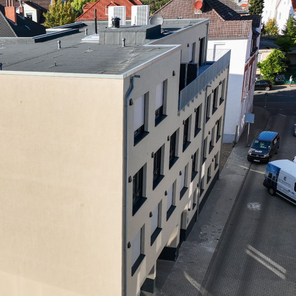 Modernes, mehrstöckiges beiges Gebäude mit technischen Installationen auf dem Dach in ruhiger Stadtumgebung.